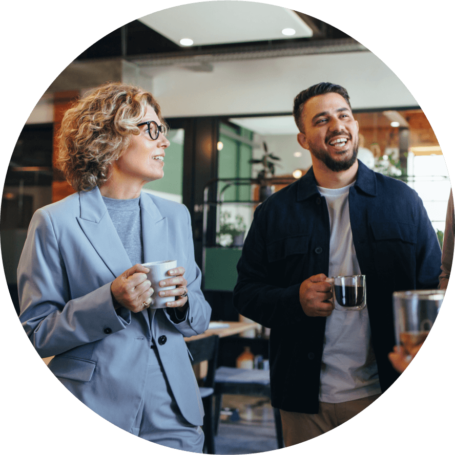 AHP staff talk over coffee. A woman in a blue suit looks towards a man in a blue jacket. A third person is just out of view, only their coffee cup is in view.